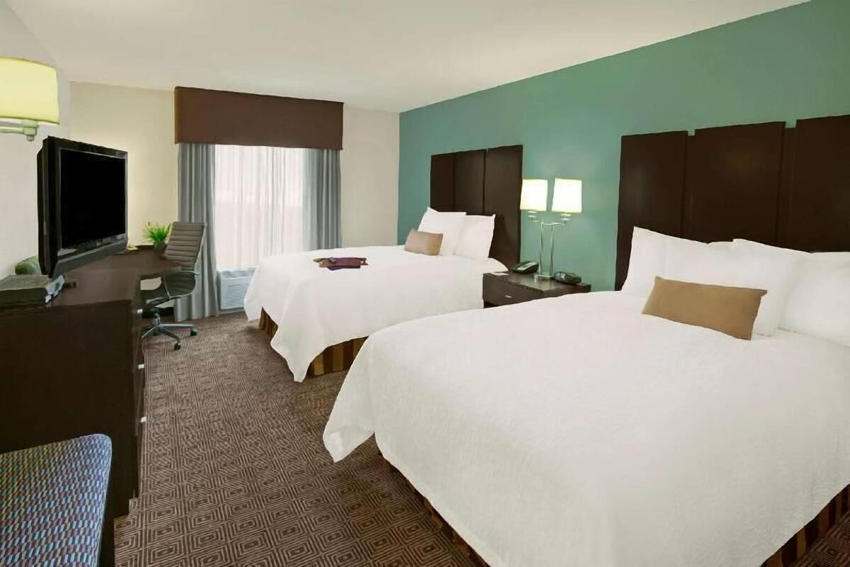 A hotel room with two beds, a desk, a television, and a window with curtains.