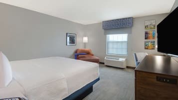 A hotel room with a large bed, a desk, a chair, a TV, and a window with a view.