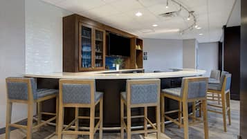 A modern bar area with a long counter, four bar stools, and a television mounted above.