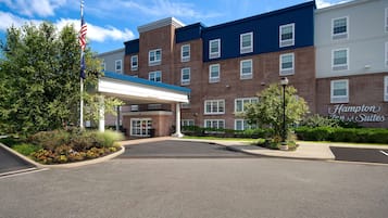 A hotel entrance with a covered walkway, brick buildings, and a sign for Hampton Inn & Suites.