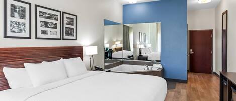 A hotel room with a large bed, a bathroom with a bathtub, and a mirror.