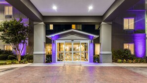 A hotel entrance with a covered entryway, a tiled walkway, and a landscaped area with trees and shrubs. - Sleep Inn & Suites Hiram - Atlanta Northwest (Hiram)
