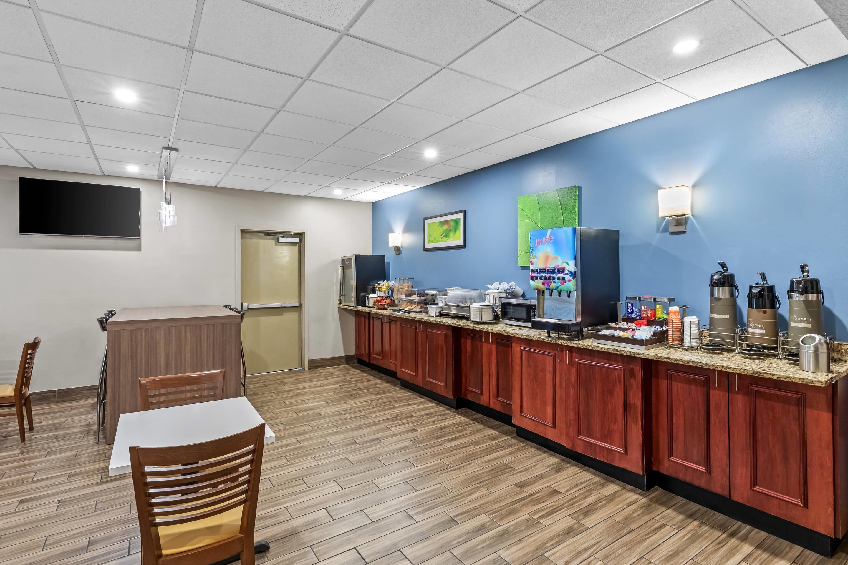 A hotel room with a kitchenette, a dining area, and a TV mounted on the wall.