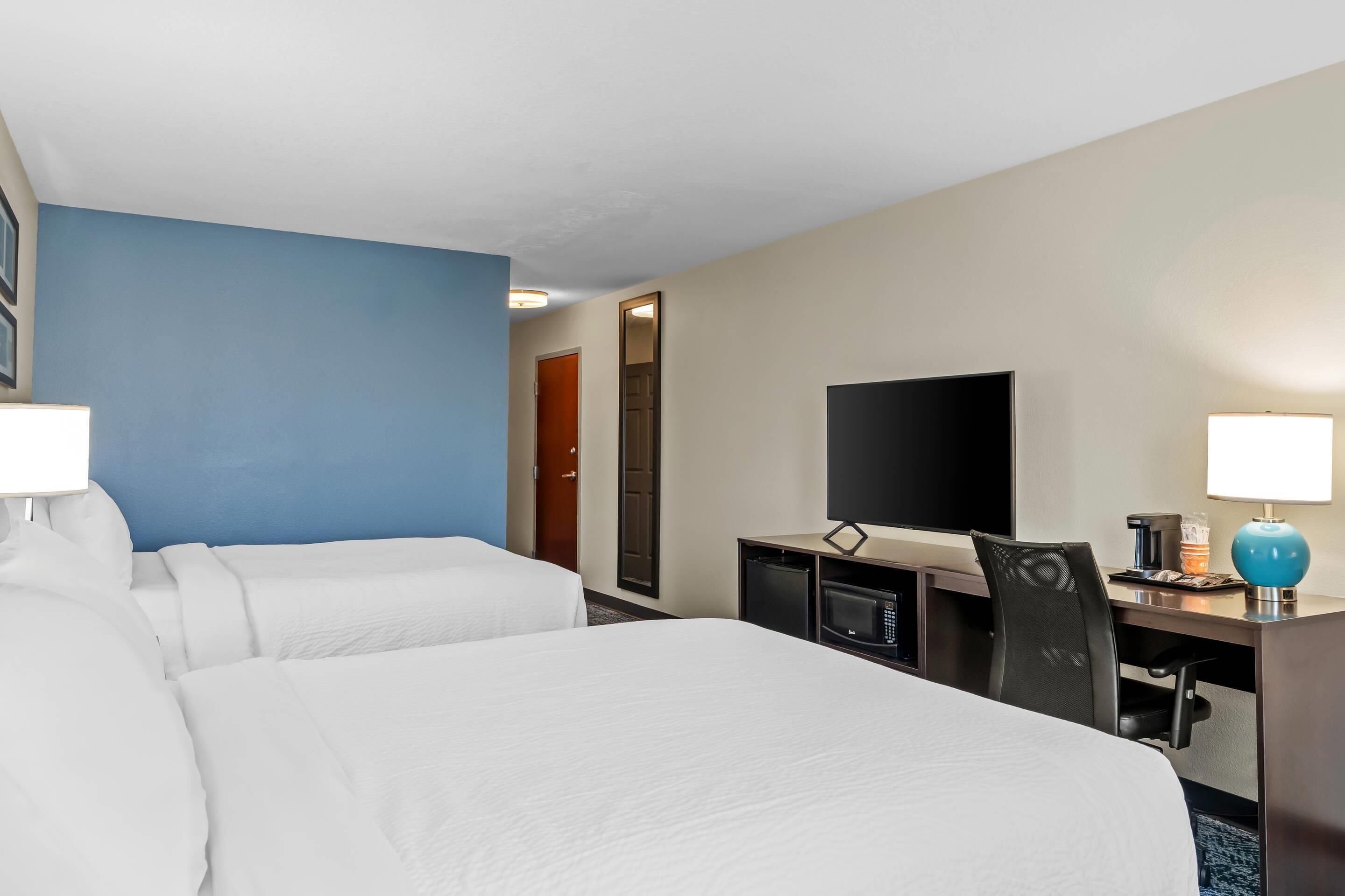 A hotel room with two beds, a desk, a television, and a coffee maker.