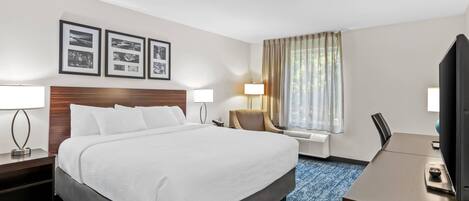 A hotel room with a large bed, a desk, a chair, a TV, and framed pictures on the wall.