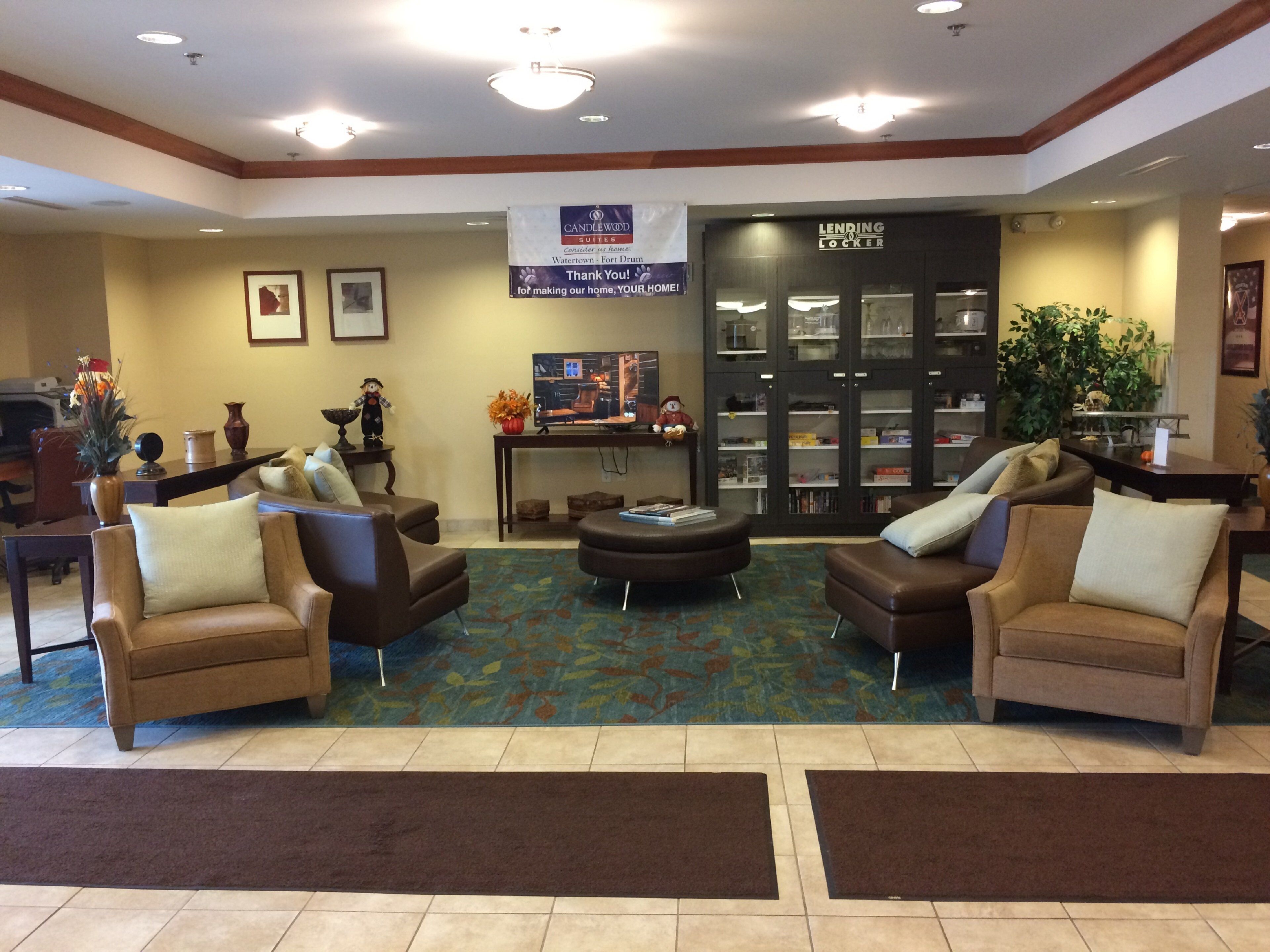 A hotel lobby with seating, a fireplace, a bookshelf, and a 'Lending Locker' sign.
