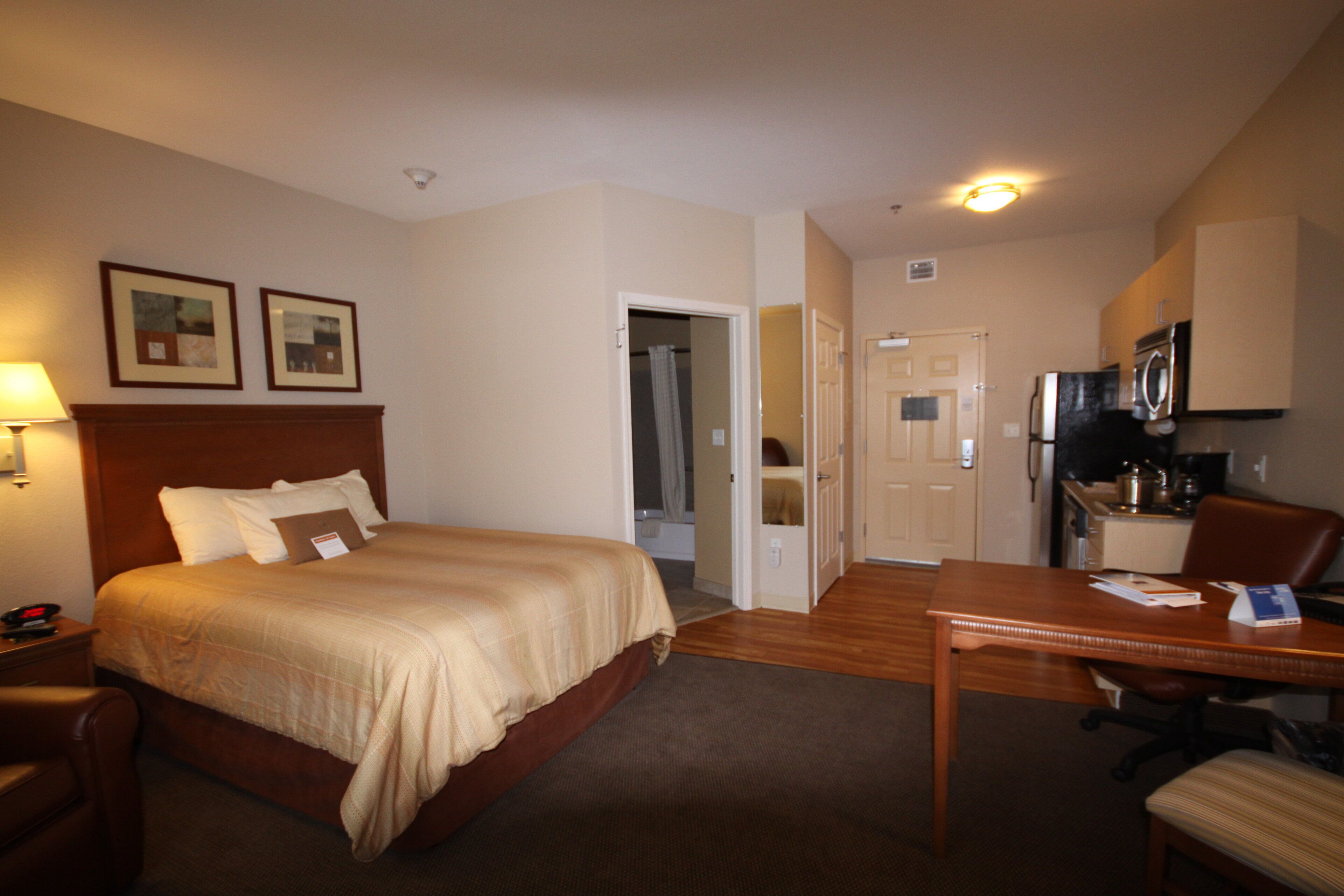 A hotel room with a bed, a desk, a chair, a microwave, and a door leading to a bathroom.