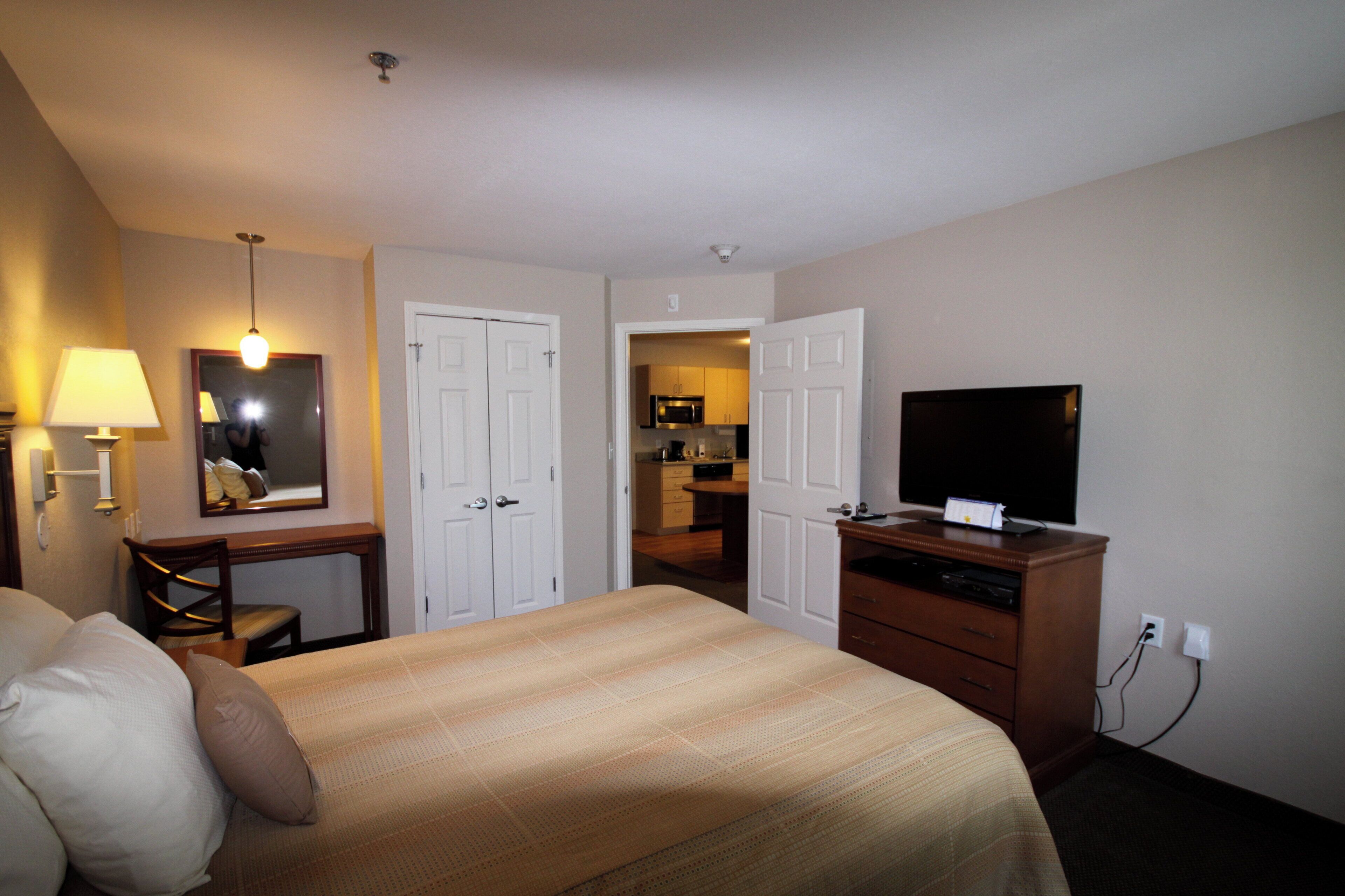 Habitación de hotel con cama, escritorio, televisor y espejo.