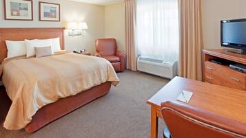 A hotel room with a bed, a chair, a desk, a television, and a window with curtains.