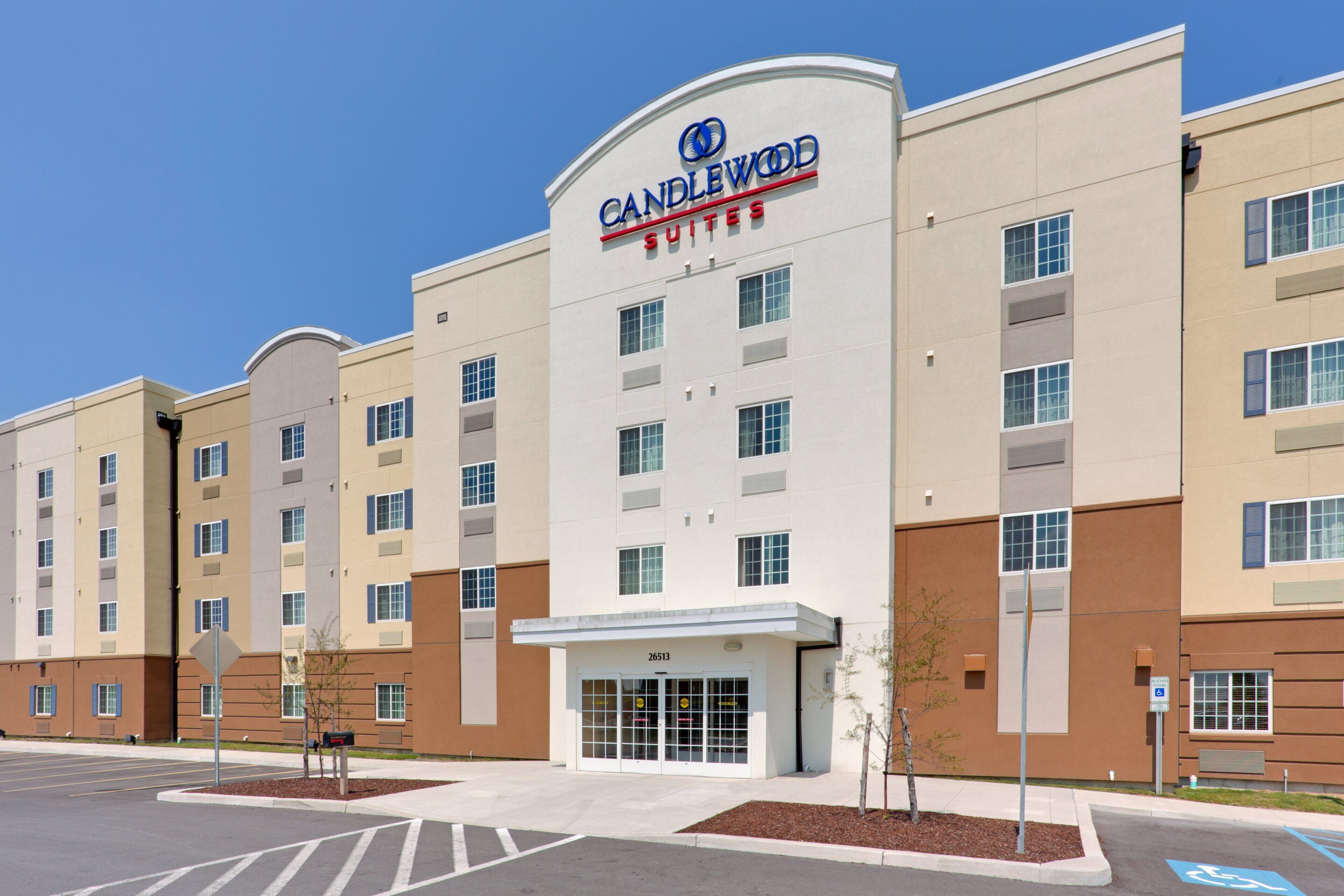 A multi-story hotel with a prominent 'Candlewood Suites' sign, a parking lot, and a clear sky.