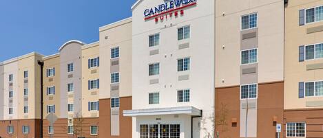 A multi-story hotel with a prominent 'Candlewood Suites' sign, a parking lot, and a clear sky.