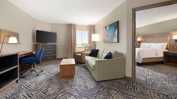 A hotel room with a flat-screen TV, a desk with a chair, a sofa, a bed, and a large mirror.