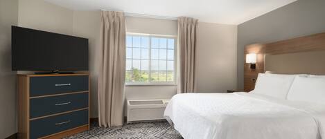 Hotelkamer met een bed, een tv op een standaard, een raam met gordijnen en een wandlamp.
