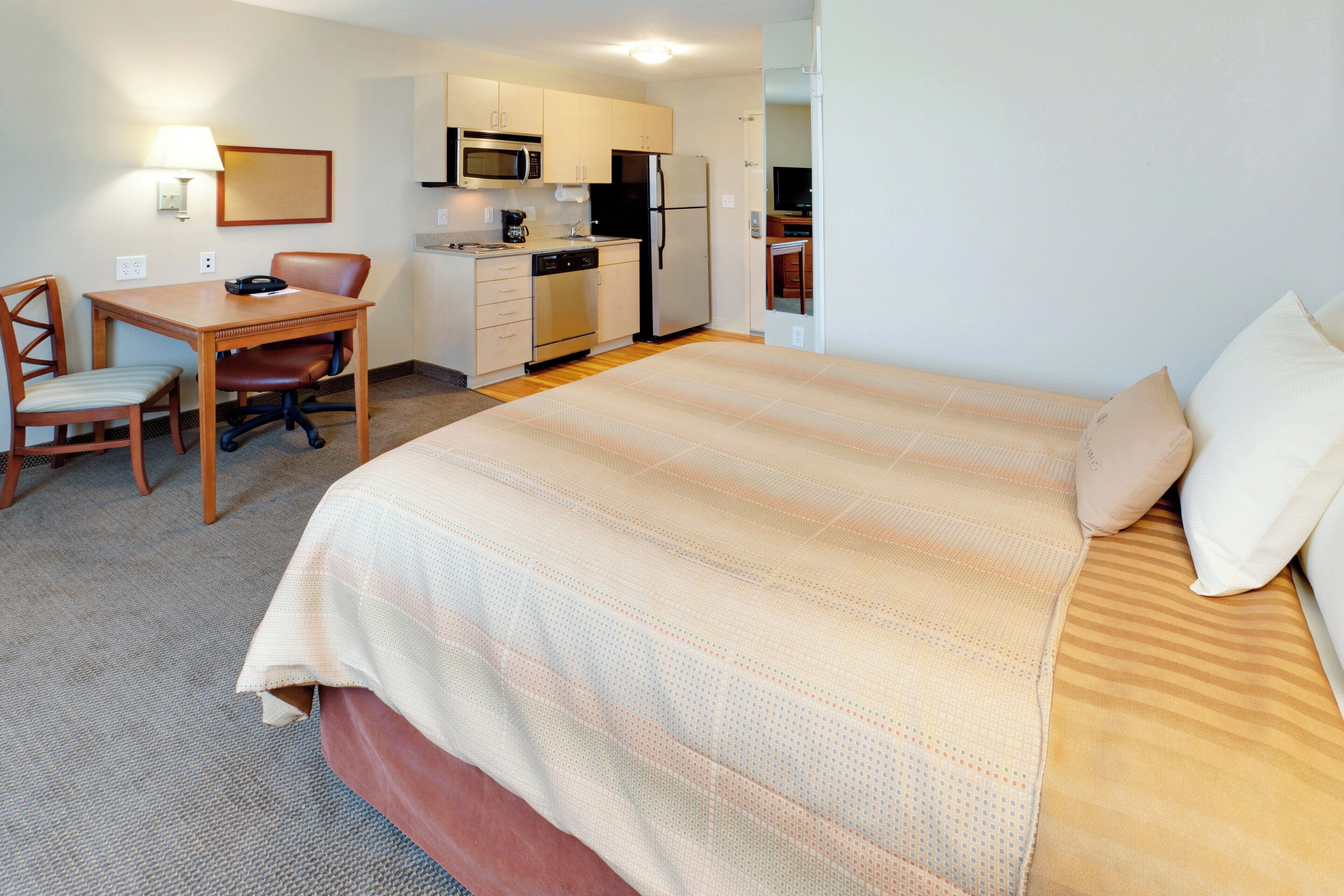 A hotel room with a bed, a desk, a chair, a microwave, a refrigerator, and a small kitchenette.