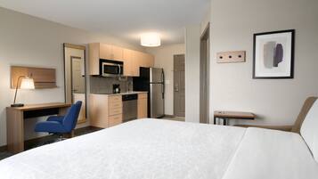 A hotel room with a bed, a desk, a chair, a kitchenette, and a small table.