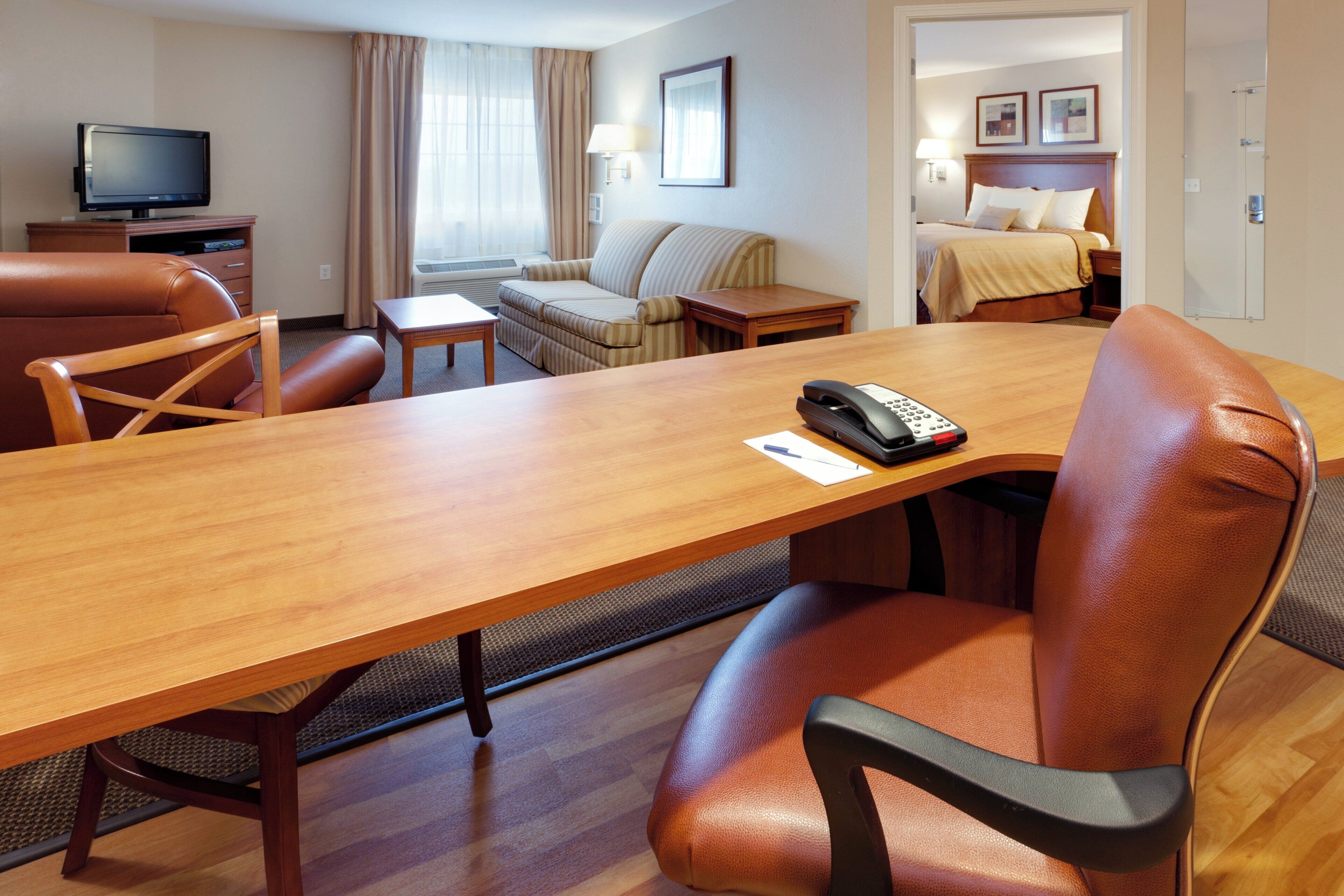 Habitación de hotel con una mesa de comedor de madera, sillas de cuero, un sofá, un televisor y una cama con cabecera.