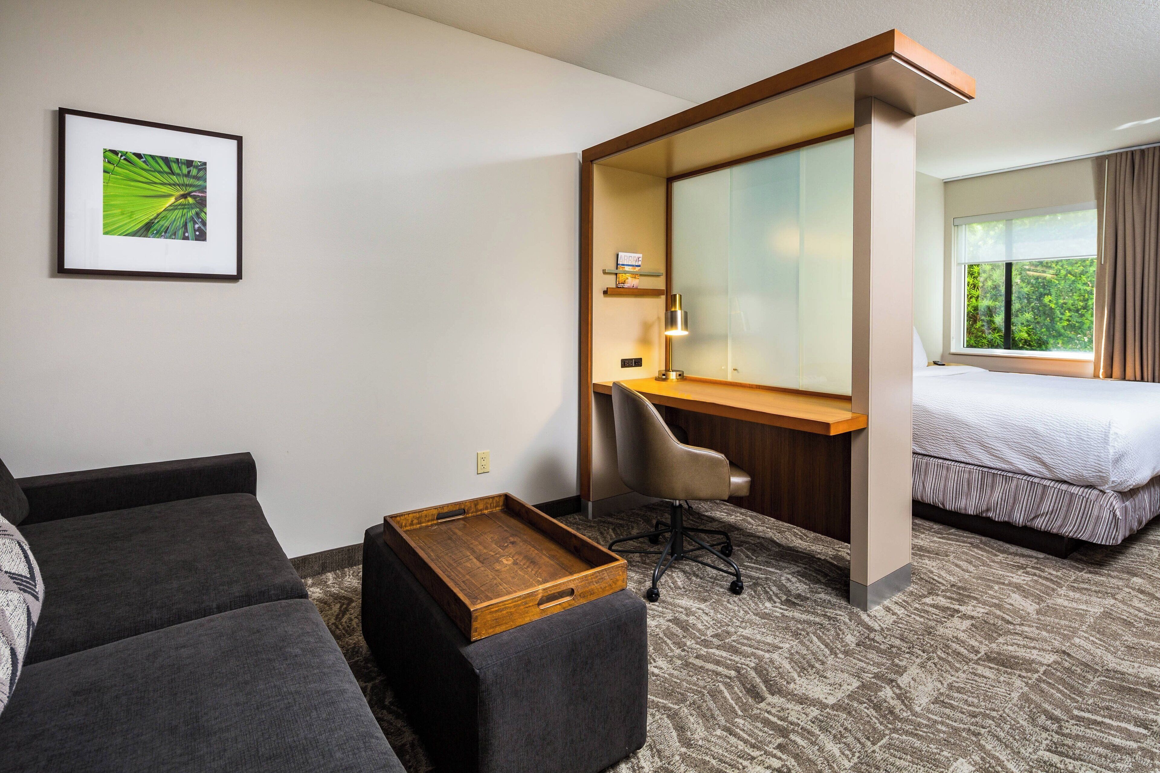 Quarto de hotel com uma cama, escrivaninha, cadeira, sofá e bandeja de madeira.