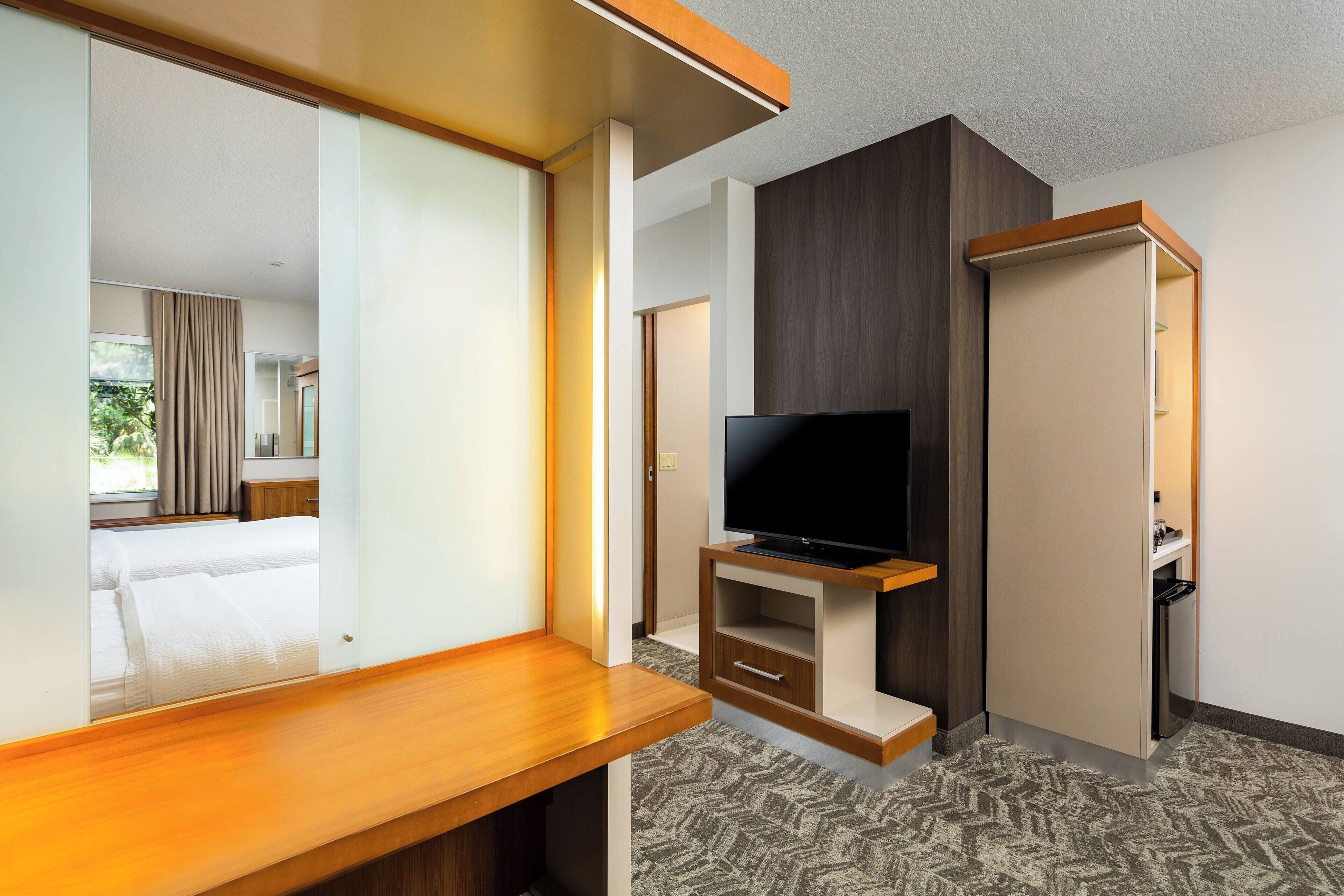 A hotel room with a wooden desk, a television, a wardrobe, and a patterned carpet.
