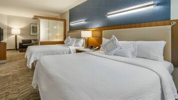 A hotel room with two beds, a desk, a chair, a lamp, and a flat-screen TV.