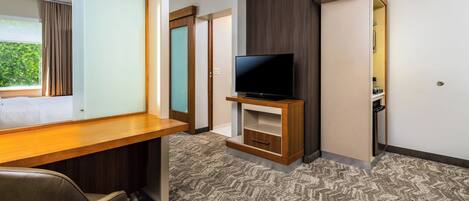 A hotel room with a wooden desk, a television on a stand, a carpeted floor, and a wardrobe.