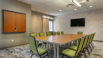 A conference room with a large table, green chairs, a projector screen, and a television on the wall.