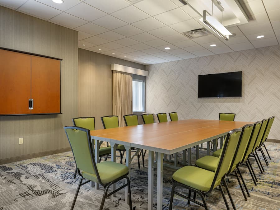 Une salle de conférence équipée d’une grande table, de chaises vertes, d’un écran de projection et d’un téléviseur fixé au mur.