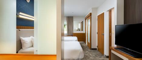 A hotel room with a bed, a TV, a desk, and a bathroom visible through an open door.