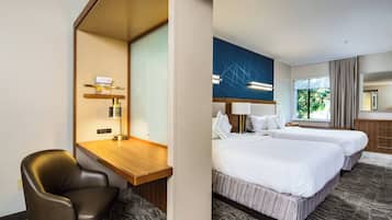 Habitación de hotel con escritorio, una silla, dos camas, un ventanal con cortinas y una pared con diseño geométrico.