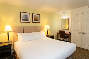 Une chambre d’hôtel avec un grand lit, deux lampes de chevet, un bureau avec une chaise et une porte.