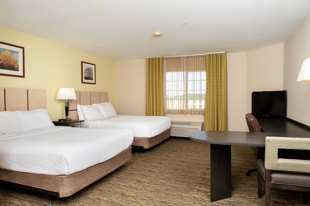 A hotel room with two beds, a desk, a chair, a television, and a window with curtains.