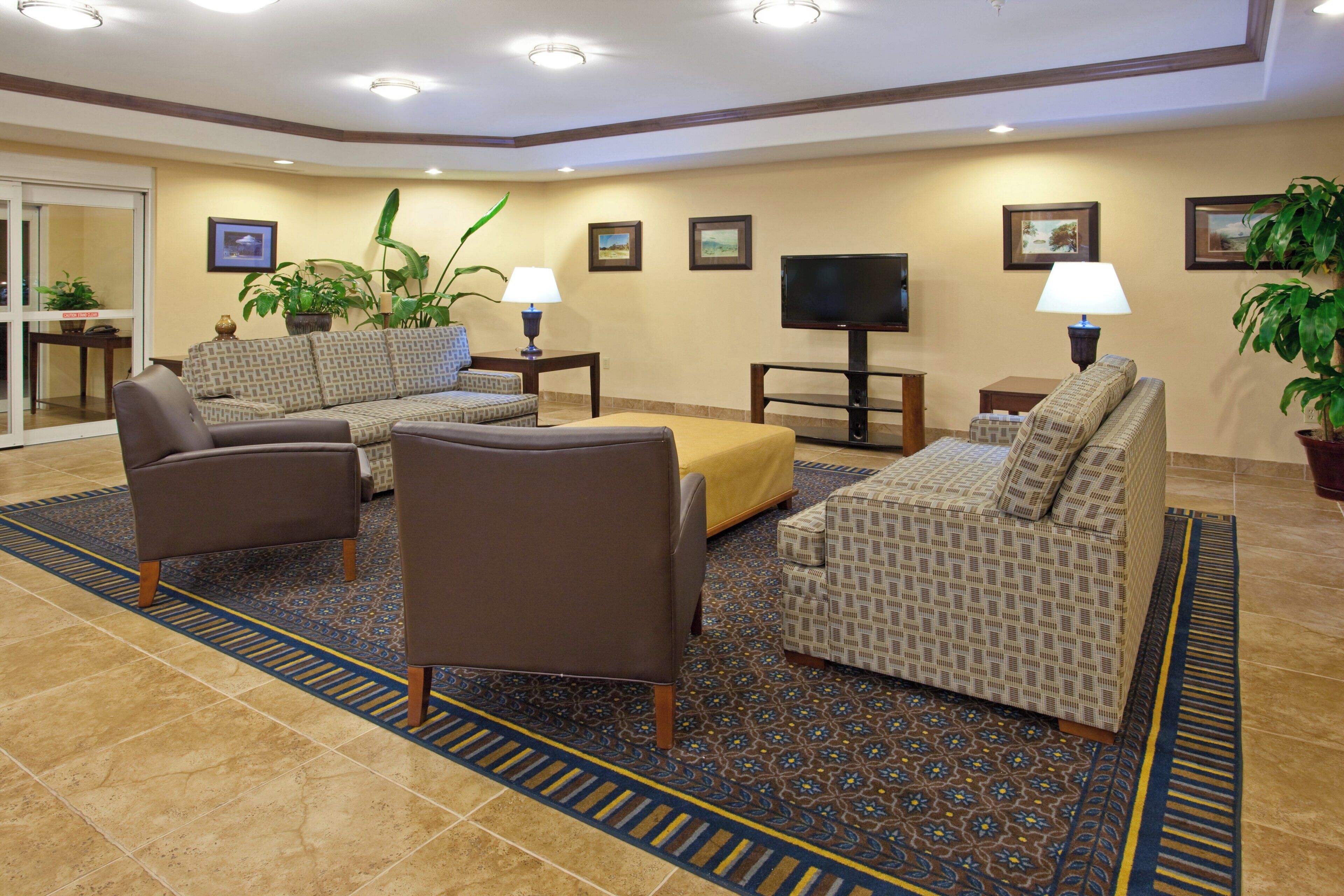 A hotel lobby with a seating area, a television, and decorative plants.