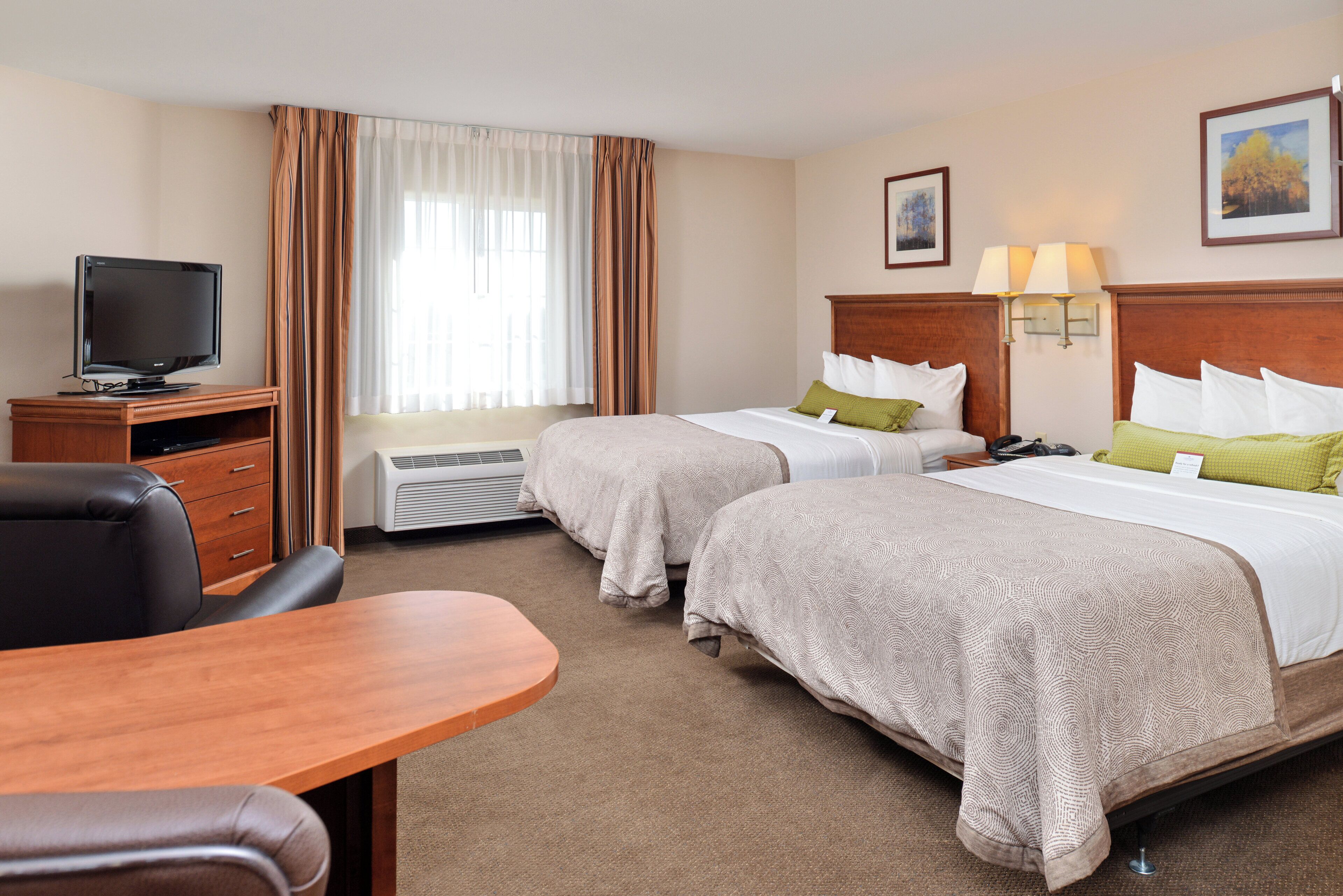 A hotel room with two beds, a desk, a television, and a window with curtains.