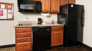 A compact kitchen with wooden cabinets, a black microwave, a black refrigerator, a dishwasher, and a coffee maker.