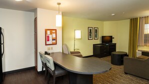 A hotel room with a dining table, two chairs, a sofa, a TV, a lamp, and a small round table.