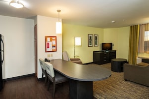 Habitación de hotel con una mesa de comedor, dos sillas, un sofá, un televisor, una lámpara y una pequeña mesa redonda.