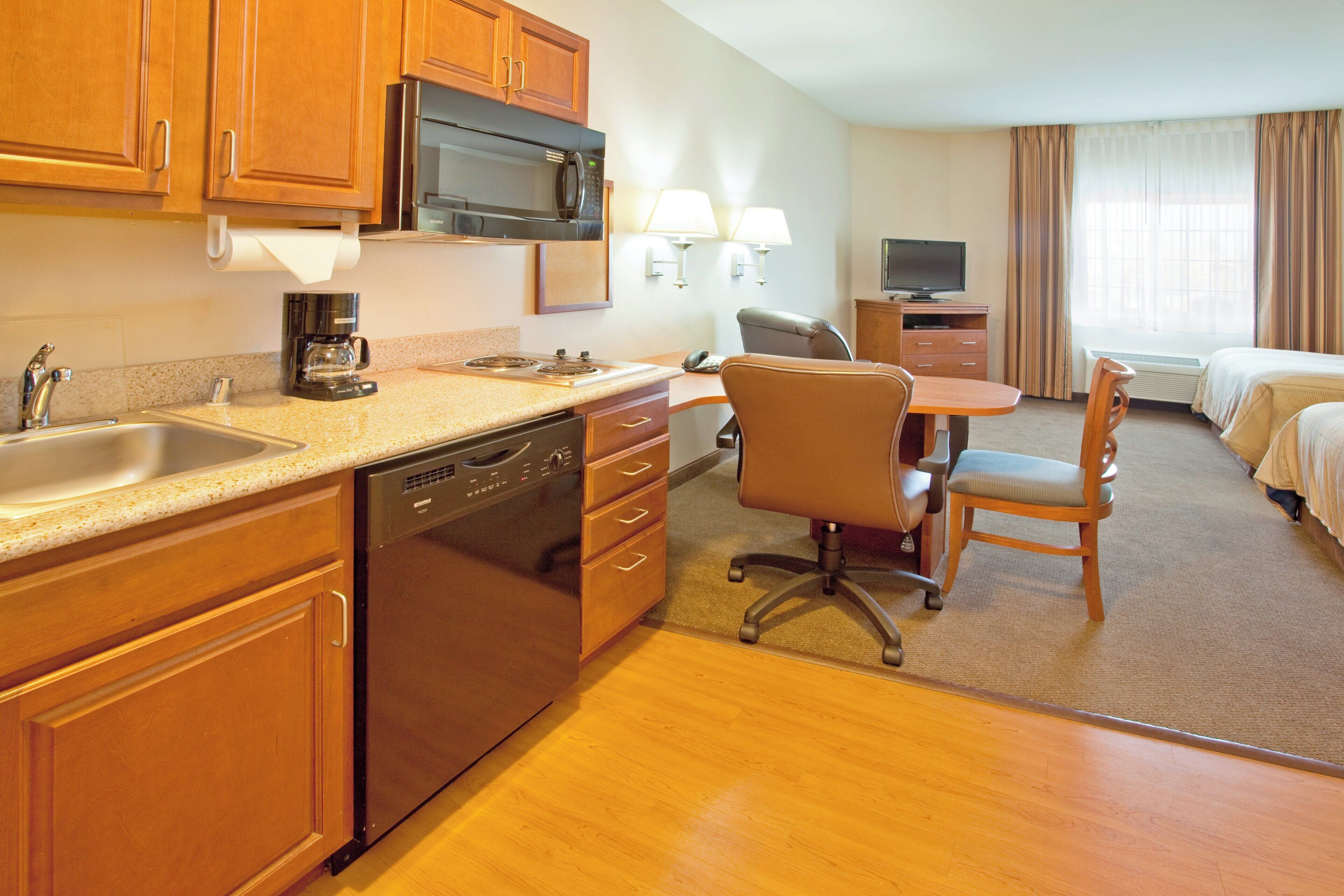 A hotel room with a kitchenette, a dining area, a bed, and a TV.