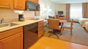A hotel room with a kitchenette, a dining area, a bed, and a TV.