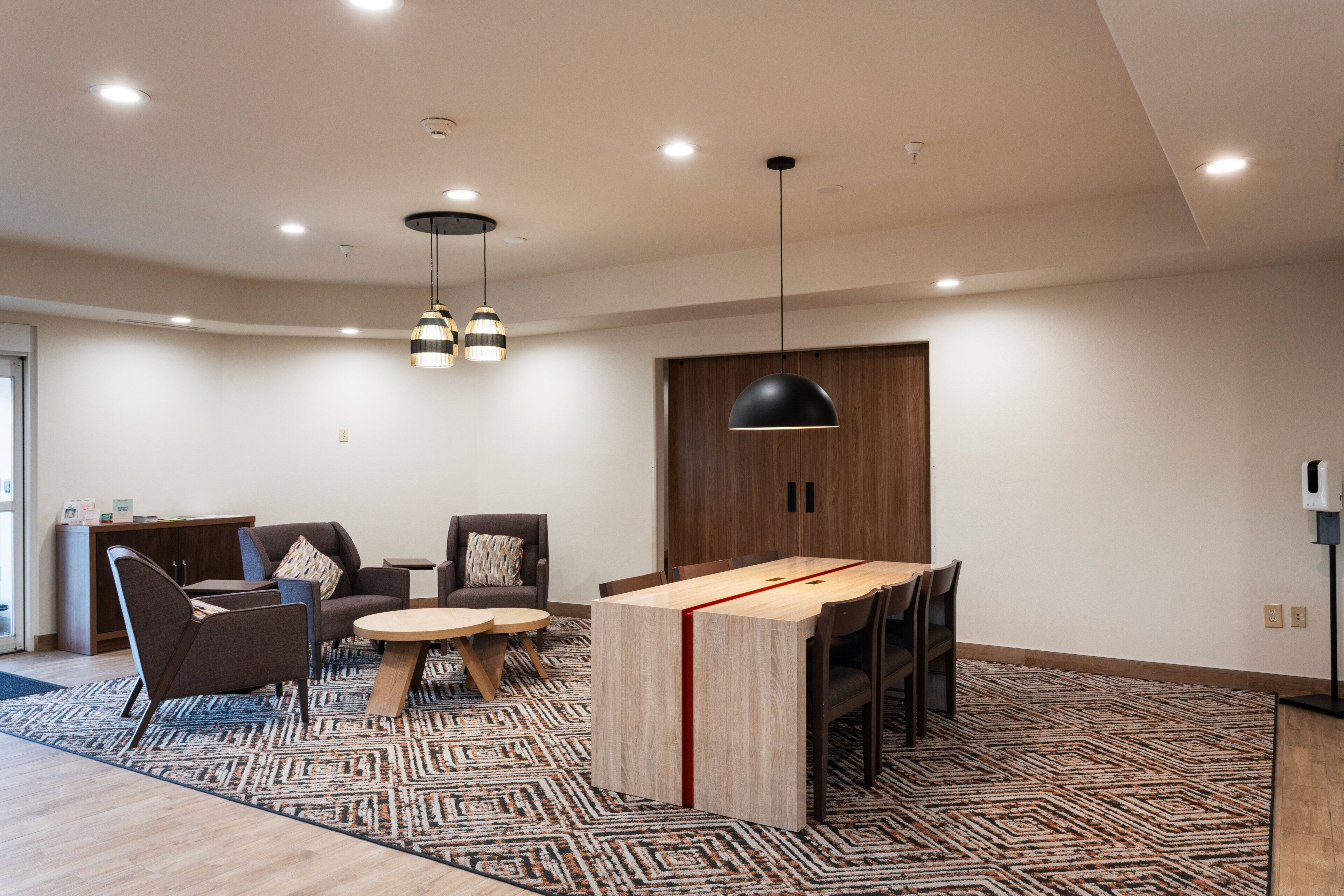 A modern living room with a dining area, featuring a wooden dining table, two sofas, and a patterned rug.