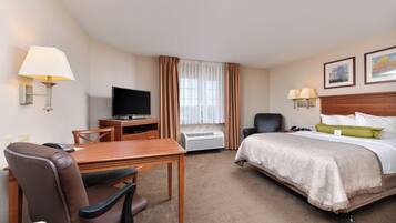 A hotel room with a bed, a desk with a television, a chair, a lamp, and a window with curtains.