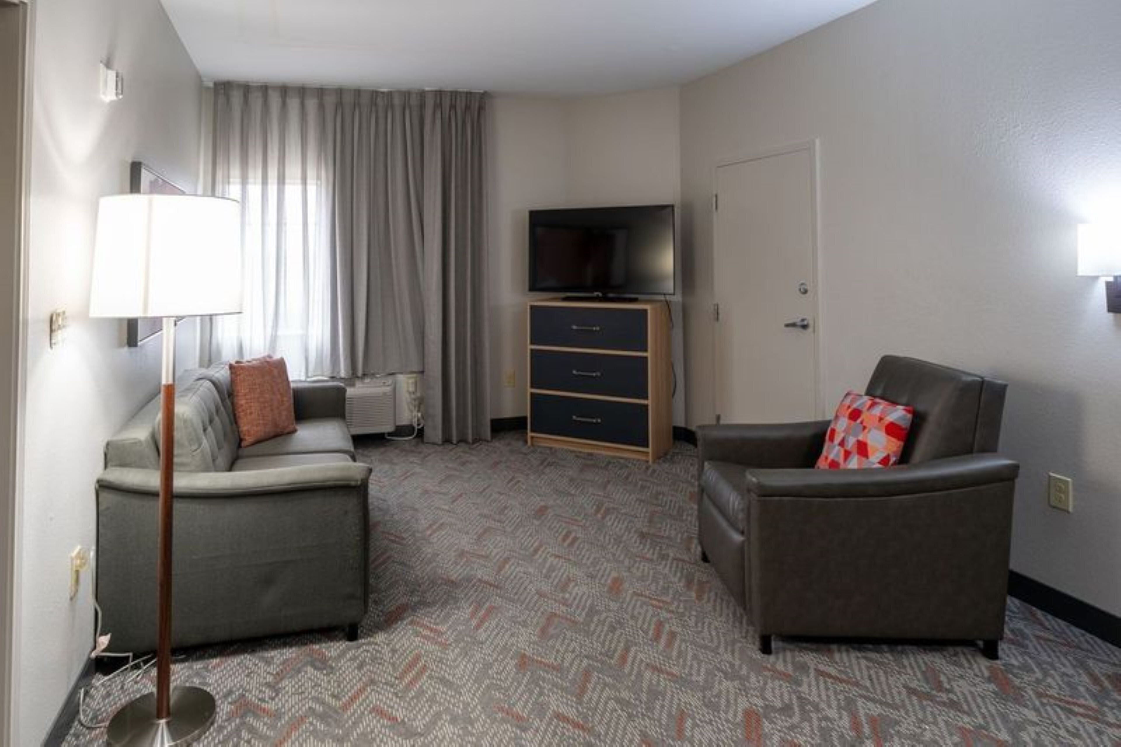 A hotel room with a sofa, a chair, a TV, a dresser, and a door.