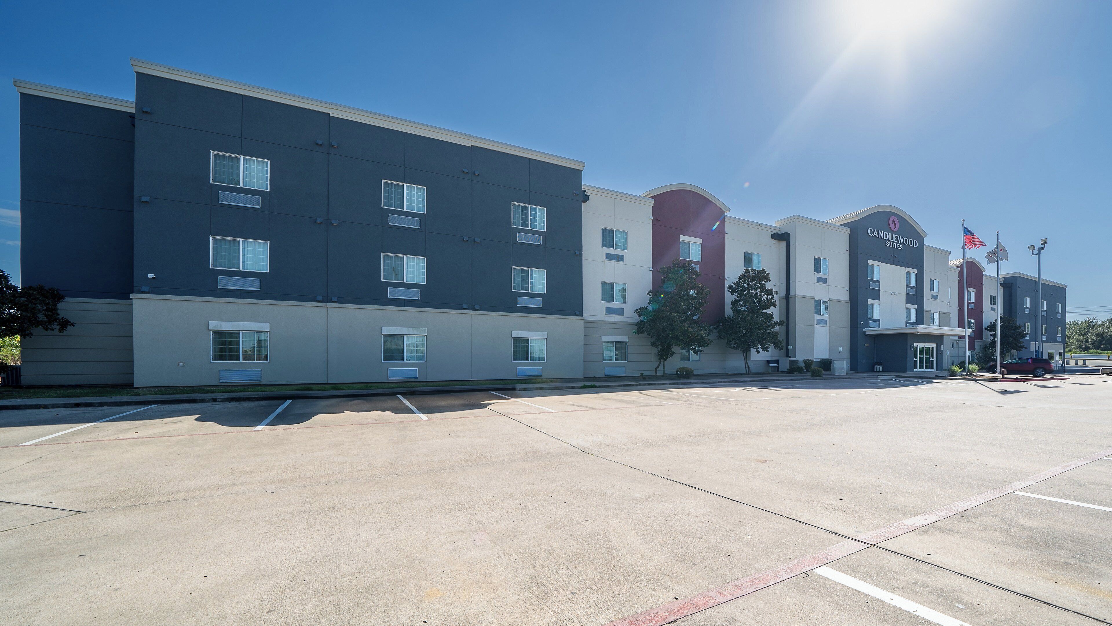 A hotel with a modern design, featuring a parking lot and a clear sky.