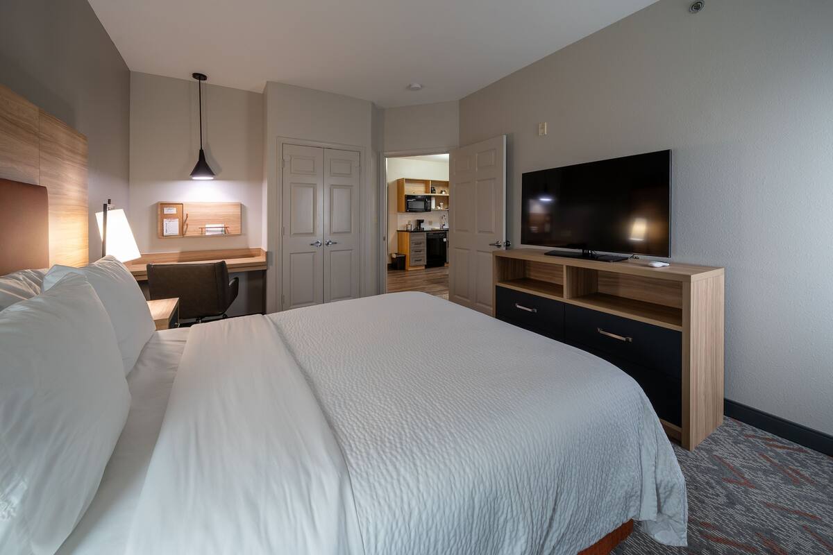 A hotel room with a large bed, a desk with a lamp, a TV on a stand, and a wardrobe.