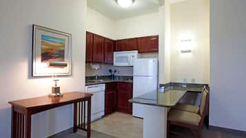 Cocina compacta con armarios de madera, microondas, refrigerador y comedor con una silla.