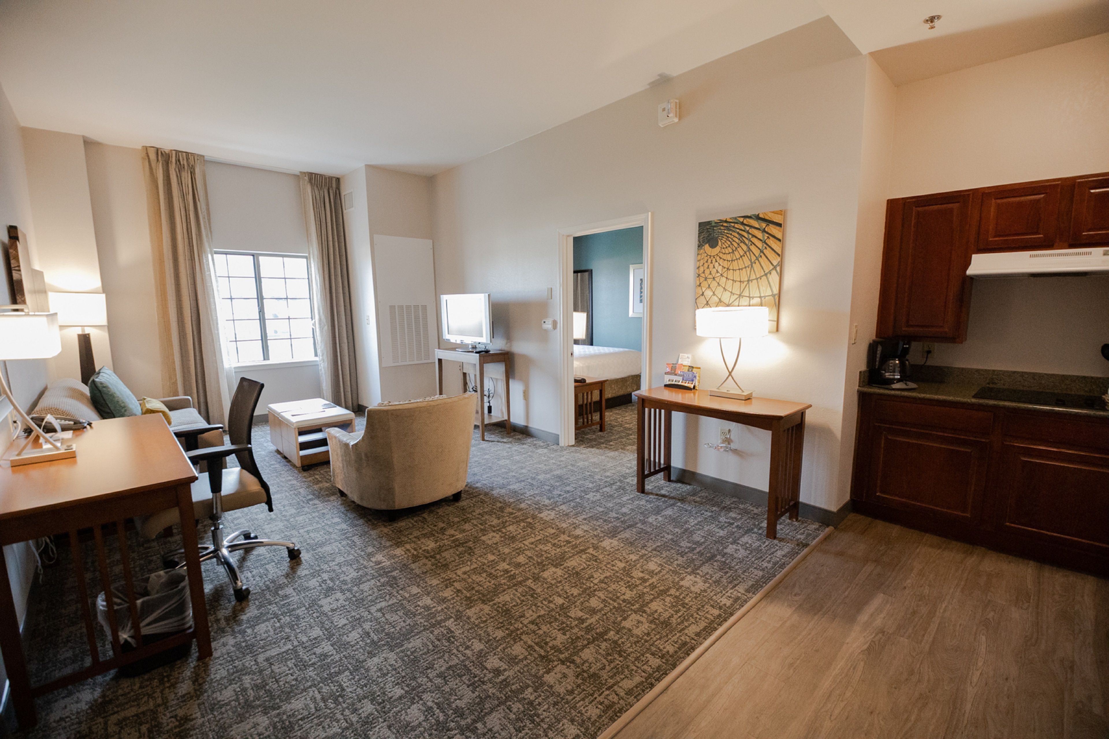 Een hotelkamer met een zithoek, een eettafel, een bank, een kitchenette en een raam met gordijnen.