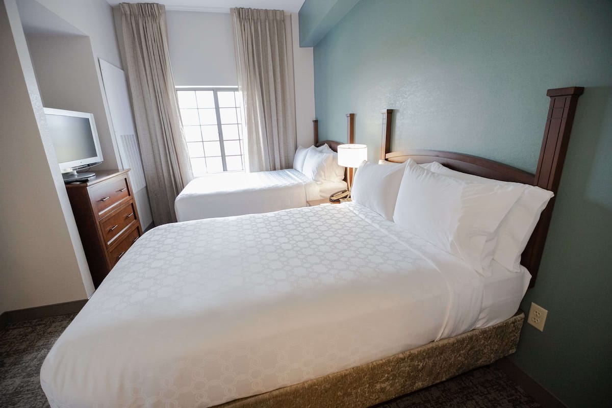 Une chambre d’hôtel avec un grand lit, une table de chevet avec une lampe, un téléviseur posé sur une commode et une fenêtre avec des rideaux.