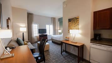 Een hotelkamer met een bed, een bureau, een stoel, een televisie, een lamp, een koffiezetapparaat en een kitchenette.