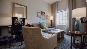 A hotel room with a desk, a chair, a sofa, a lamp, and a window with curtains. - Sonesta ES Suites Baton Rouge University at Southgate (Baton Rouge)
