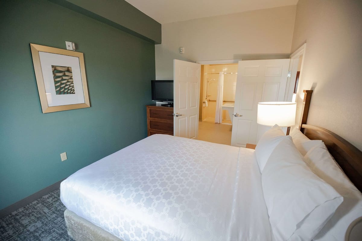 Une chambre d’hôtel avec un lit soigneusement fait, un téléviseur posé sur une commode et une salle de bain visible à travers une porte ouverte.