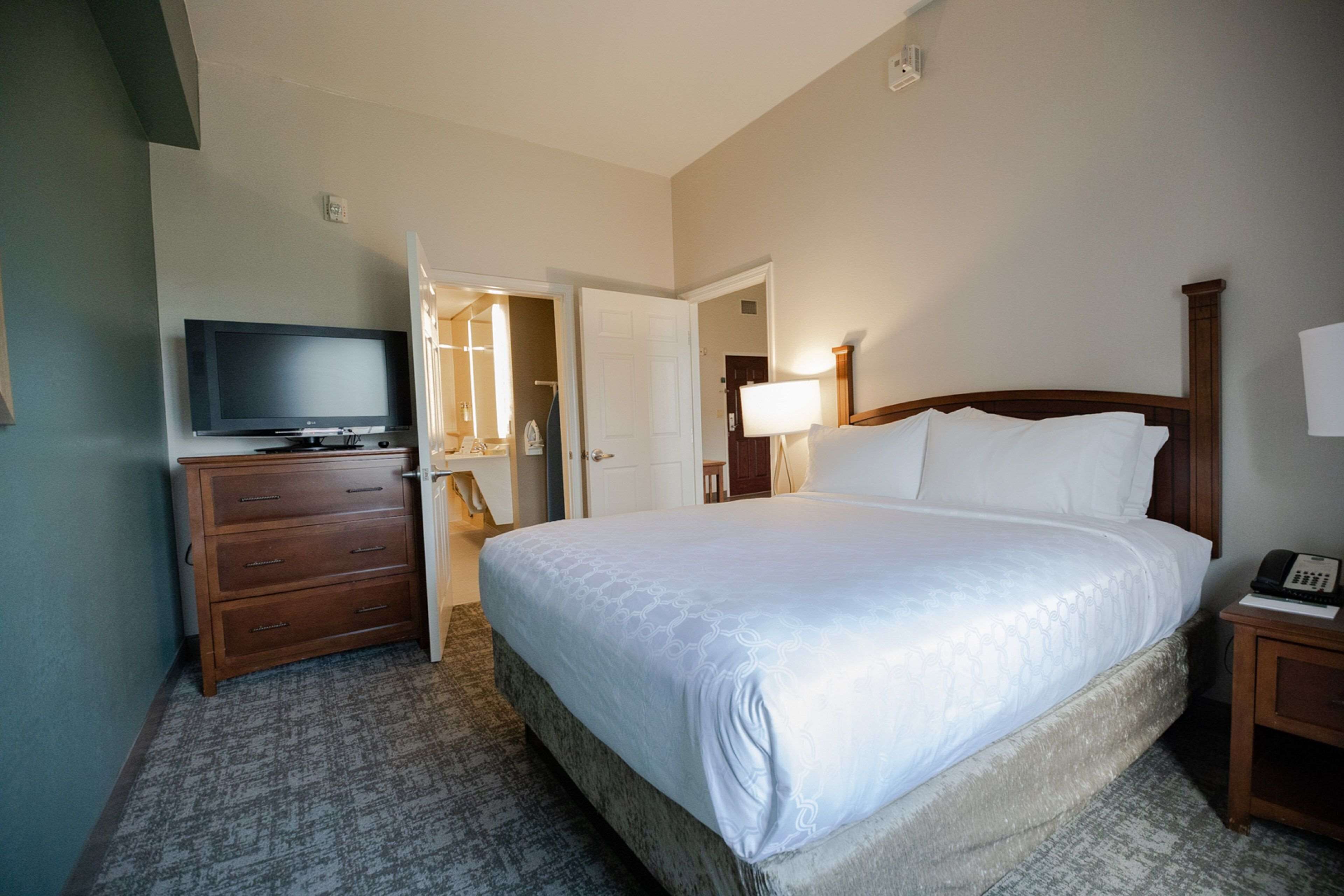 Habitación de hotel con una cama grande, un televisor sobre una cómoda de madera, una lámpara de noche y un teléfono en una mesita.