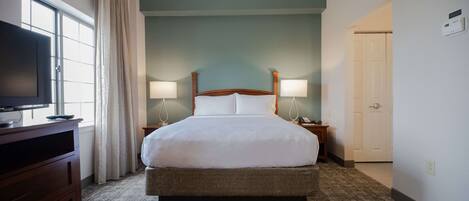 Habitación de hotel con una cama grande, dos lámparas de noche, un televisor en una cómoda y una ventana con cortinas.